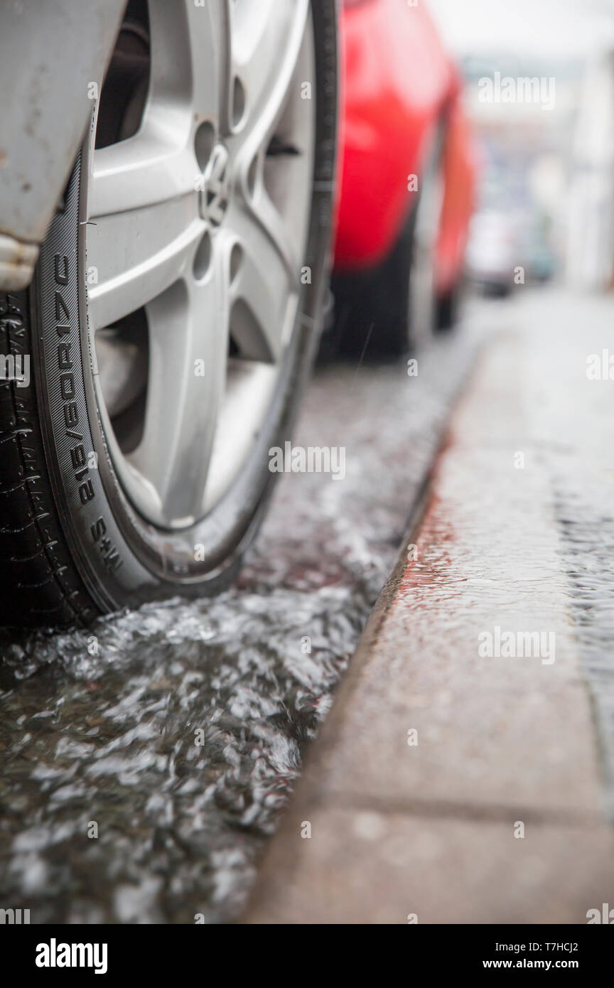 Vertical, close-up, worm's-eye view of vehicle tyre in flood water parked at kerbside of UK road. Stock Photo