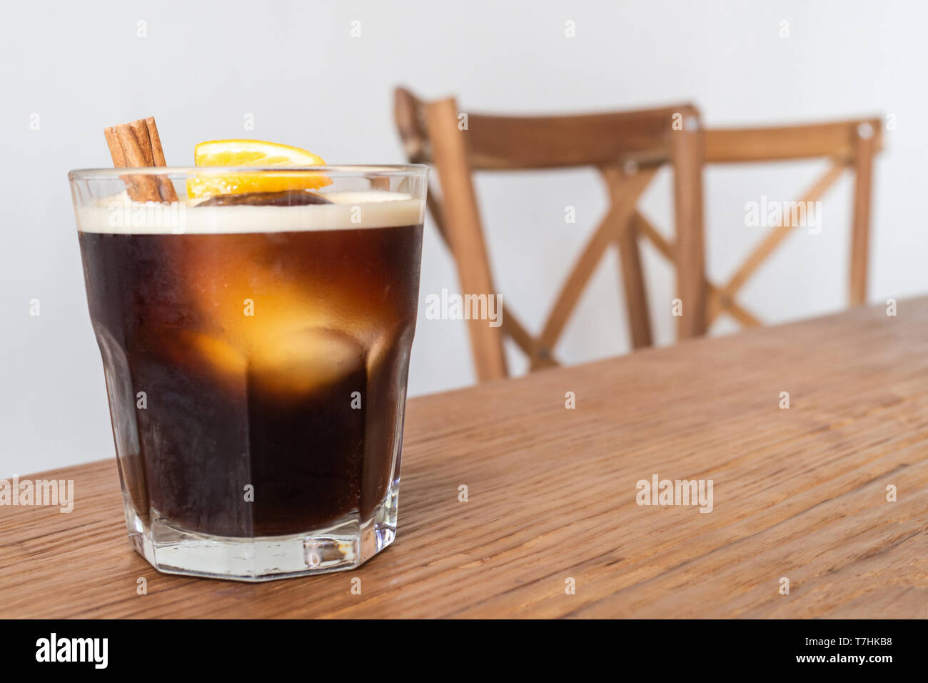 nitro cold brew coffee with ice, cinnamon and lemon on wooden table and chairs set as a special drink menu ready to serve for the client on the coffee Stock Photo