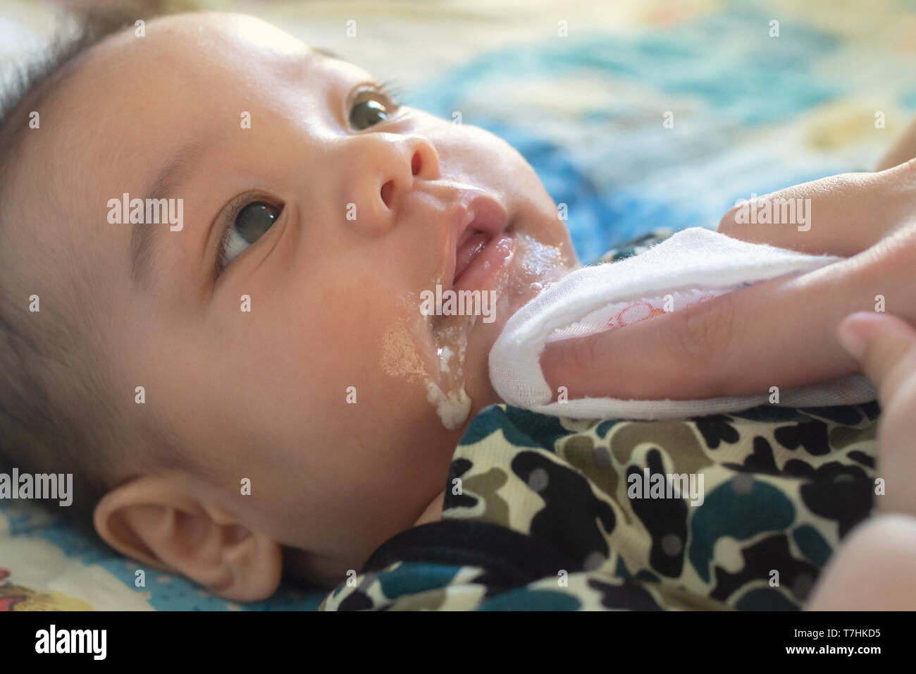 asian mother is wiping her baby's face after infant baby boy vomiting with soft sunbeam. people and family lifestyle concept. Stock Photo