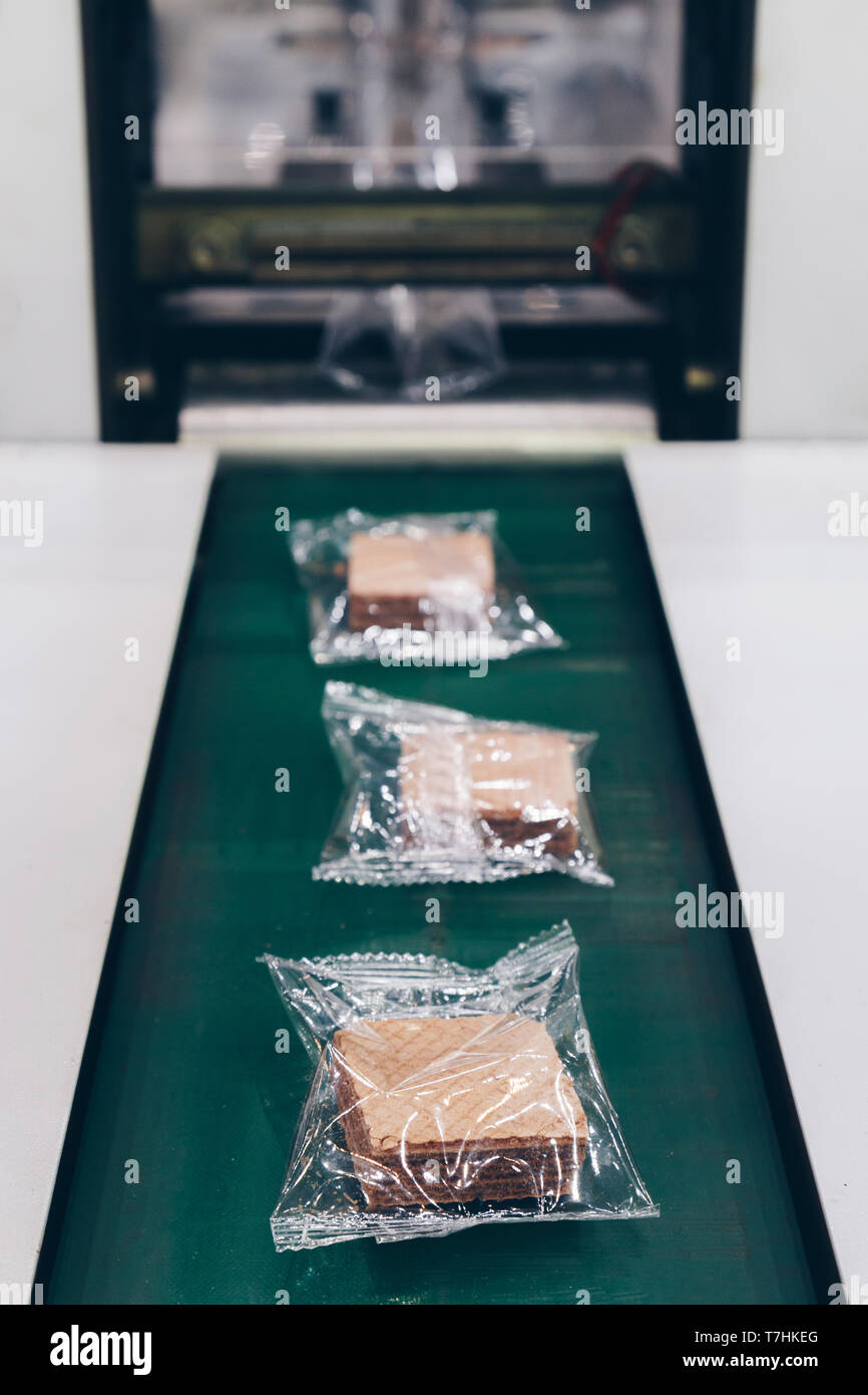 crispy wafer biscuits packing in the plastic back in production line on the conveyor belt of automatic packing machine at bakery factory. food industr Stock Photo