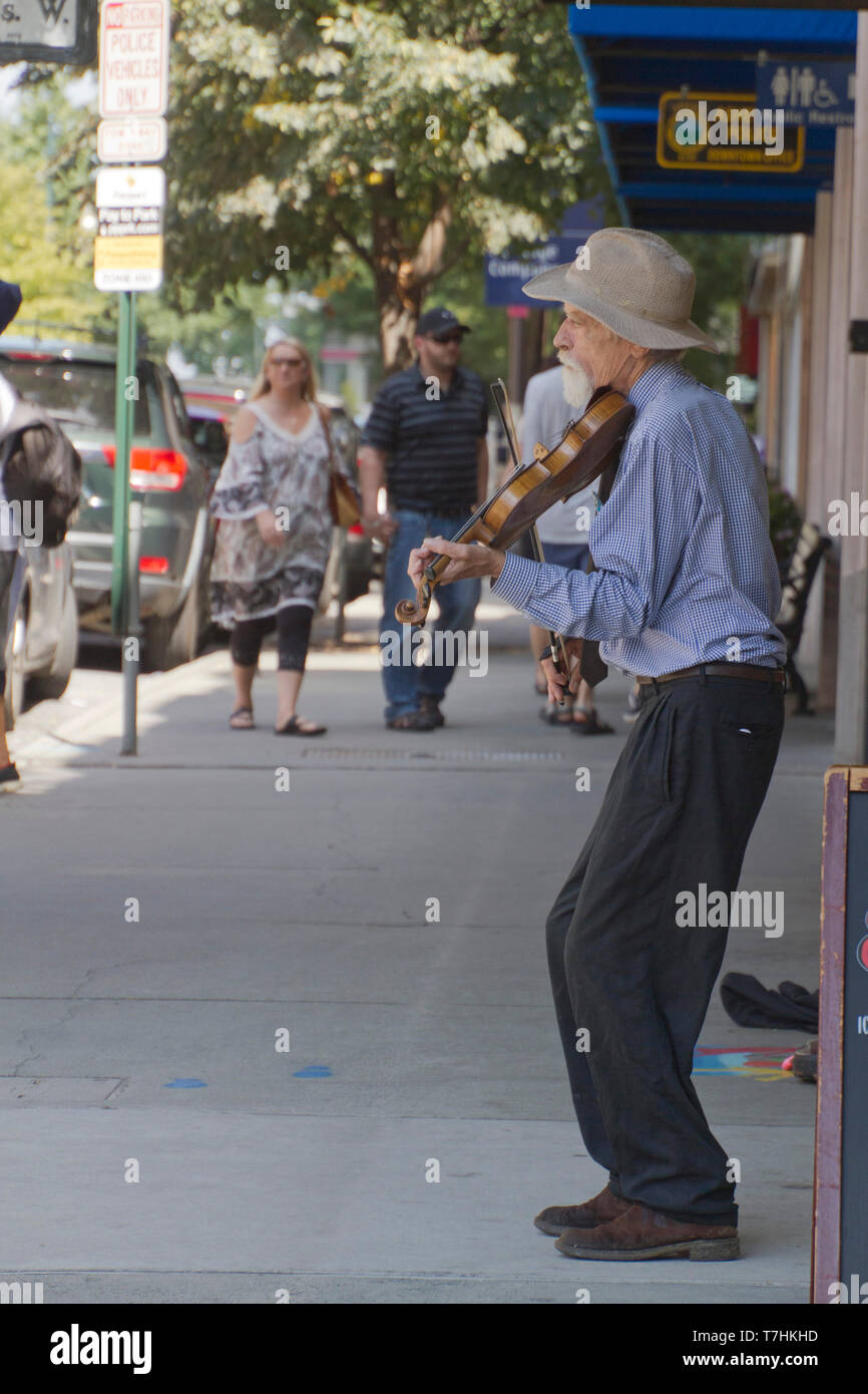 ASHEVILLE, NORTH CAROLINA, USA - September 9, 2018: An older violin player plays solo for tips on a busy downtown Asheville street next to a sign comm Stock Photo