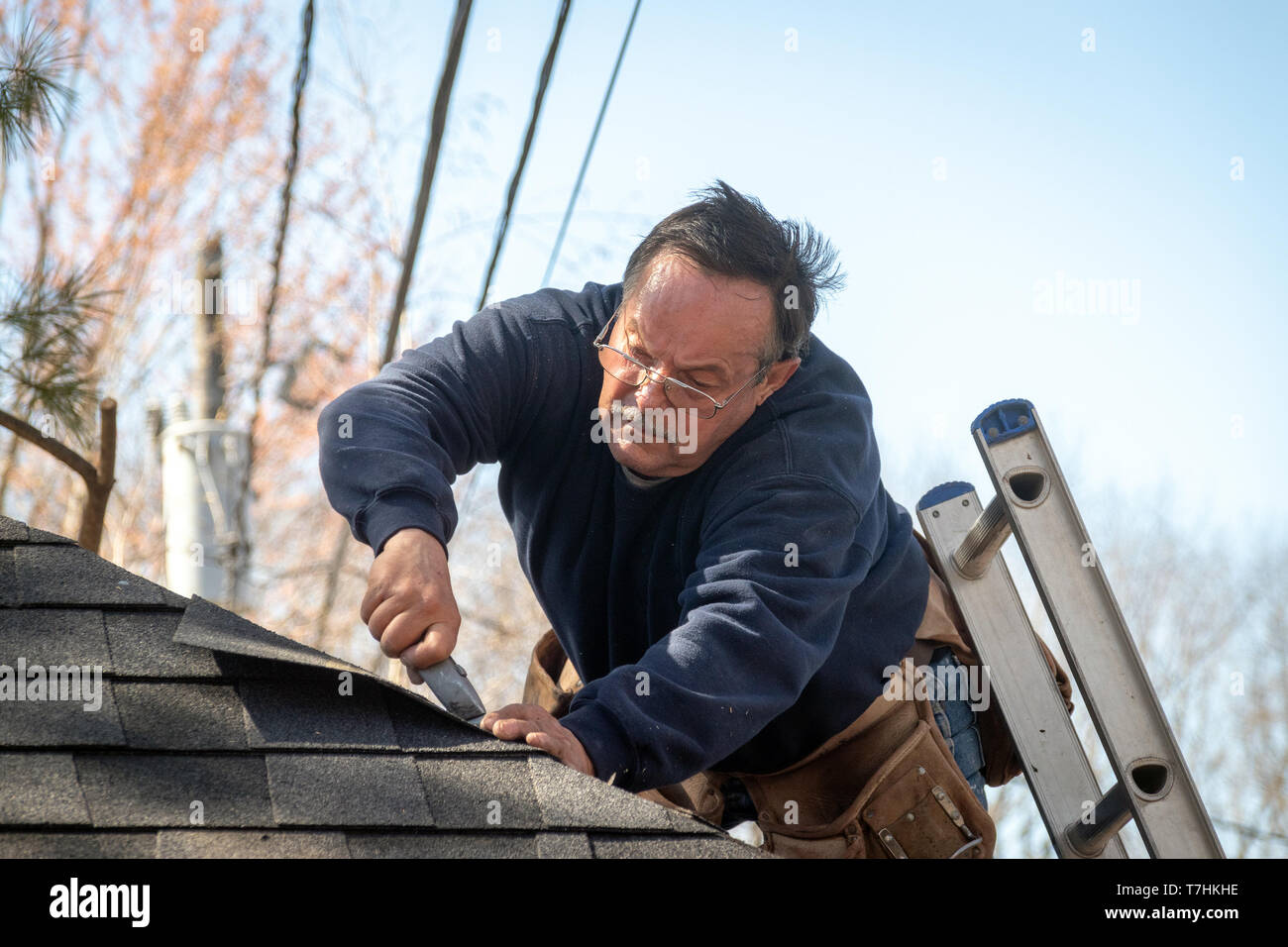 60 years old roofer putting asphalt roof shingles on a house structure Stock Photo