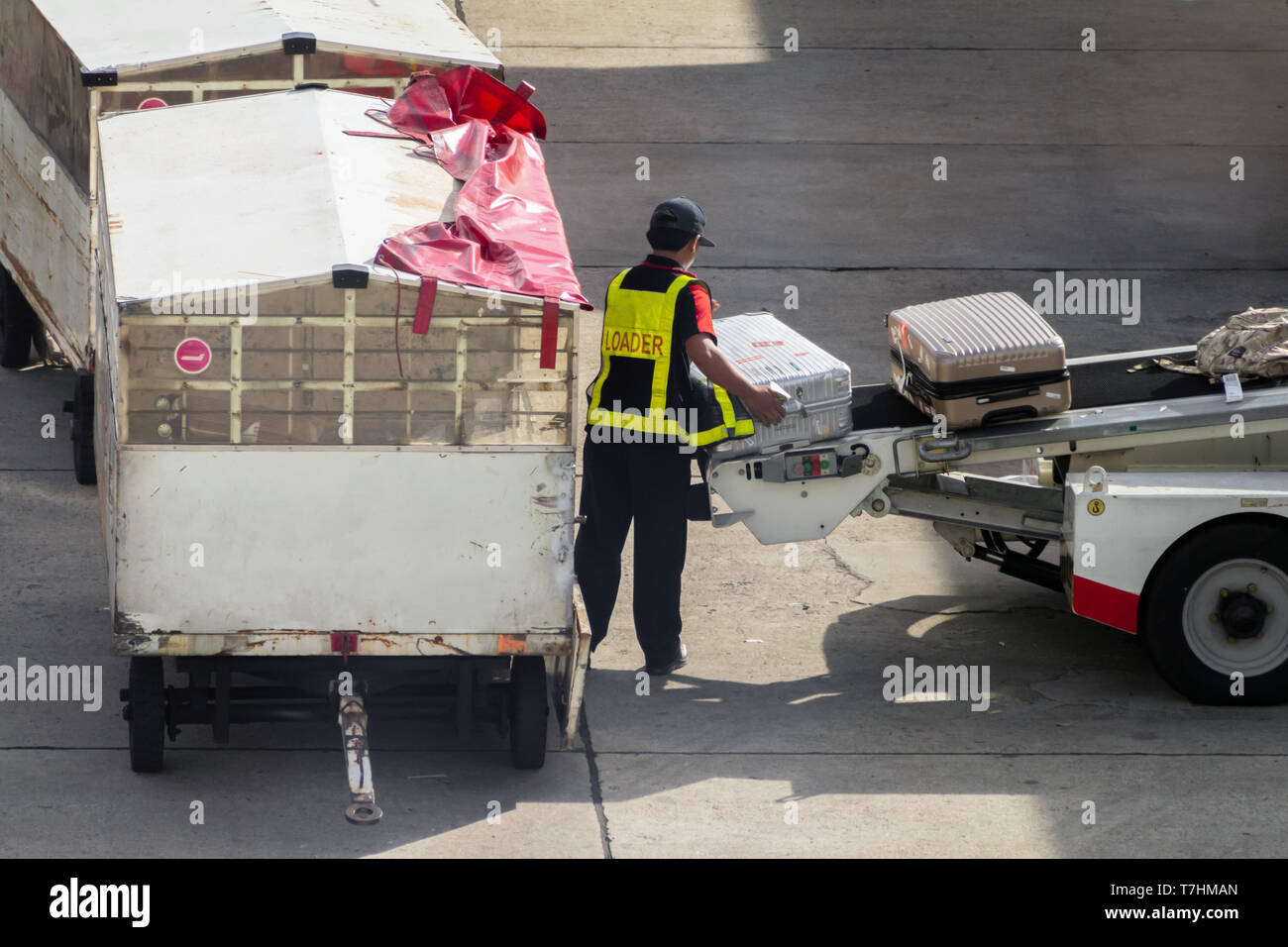 asian man loader lifting up the luggage to conveyor belt of the trailer to loading passenger baggage to the airplane on the runway at the airport. tra Stock Photo