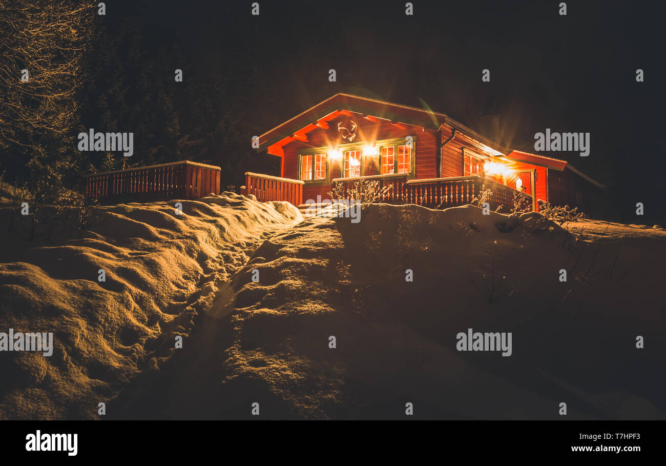 Red wooden cabin in wintertime. Night lights and snow covered ground. Stock Photo