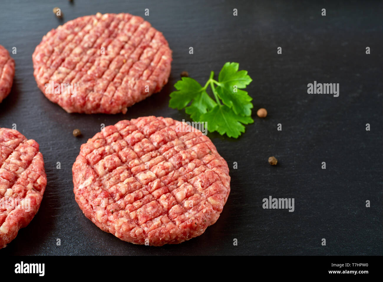 Raw beef patties with spices on black slate Stock Photo
