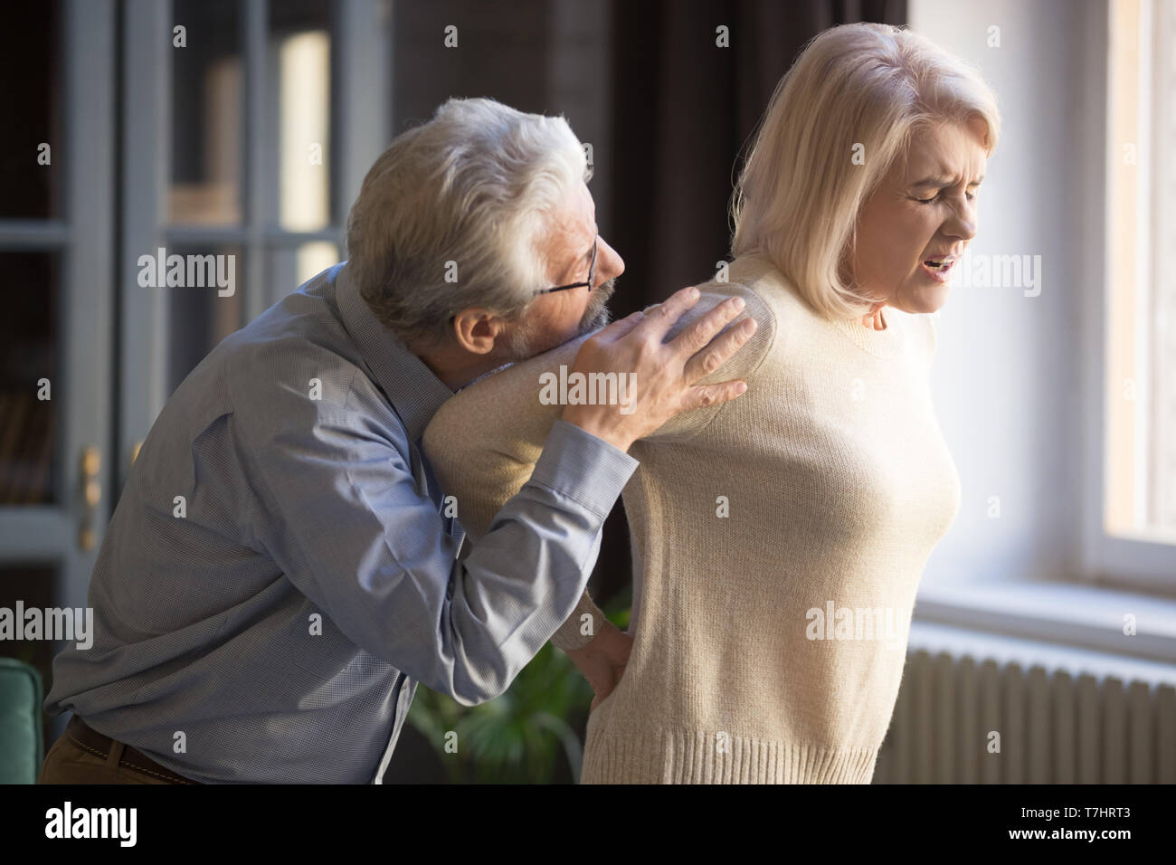 Mature woman suffering from sudden backache, old man supporting her Stock Photo