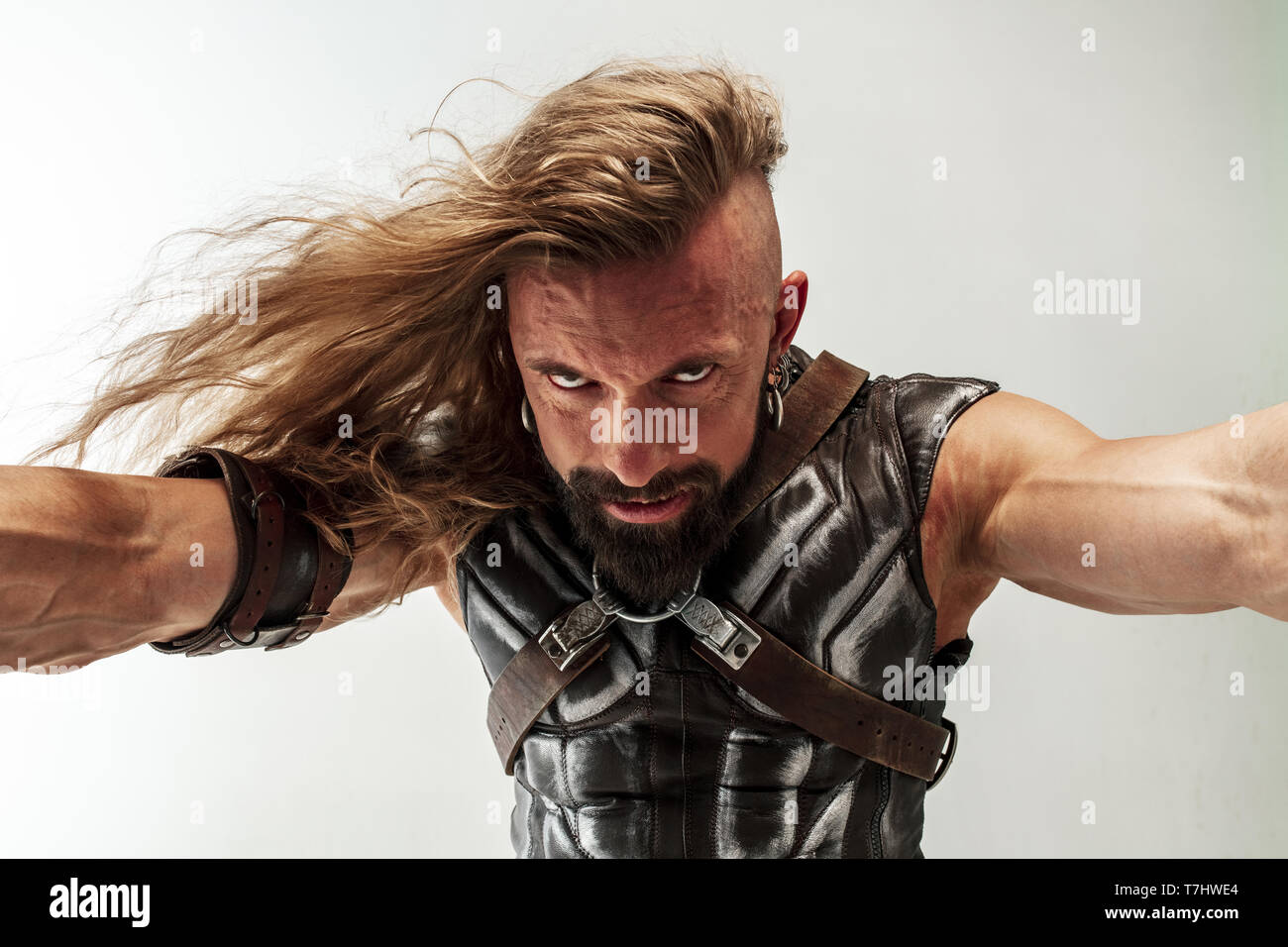 God of thunder. Blonde long hair and muscular male model in leather  viking's costume with the big hammer cosplaying Thor isolated on white  studio background. Fantasy warrior, antique battle concept Stock Photo -
