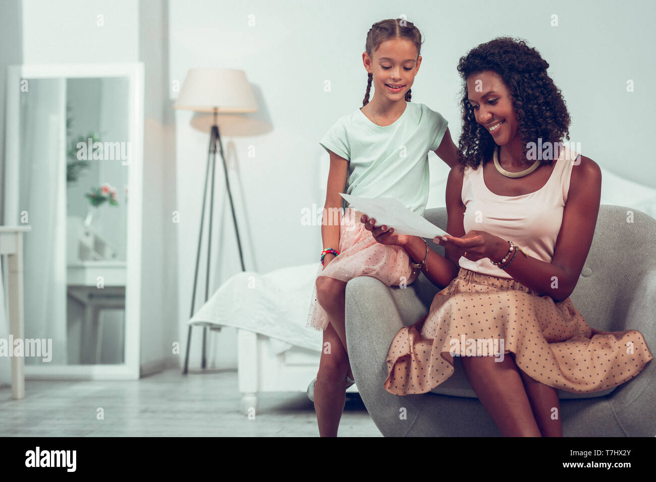 Glowing Afro-American mother looking at the drawing of daughter. Stock Photo