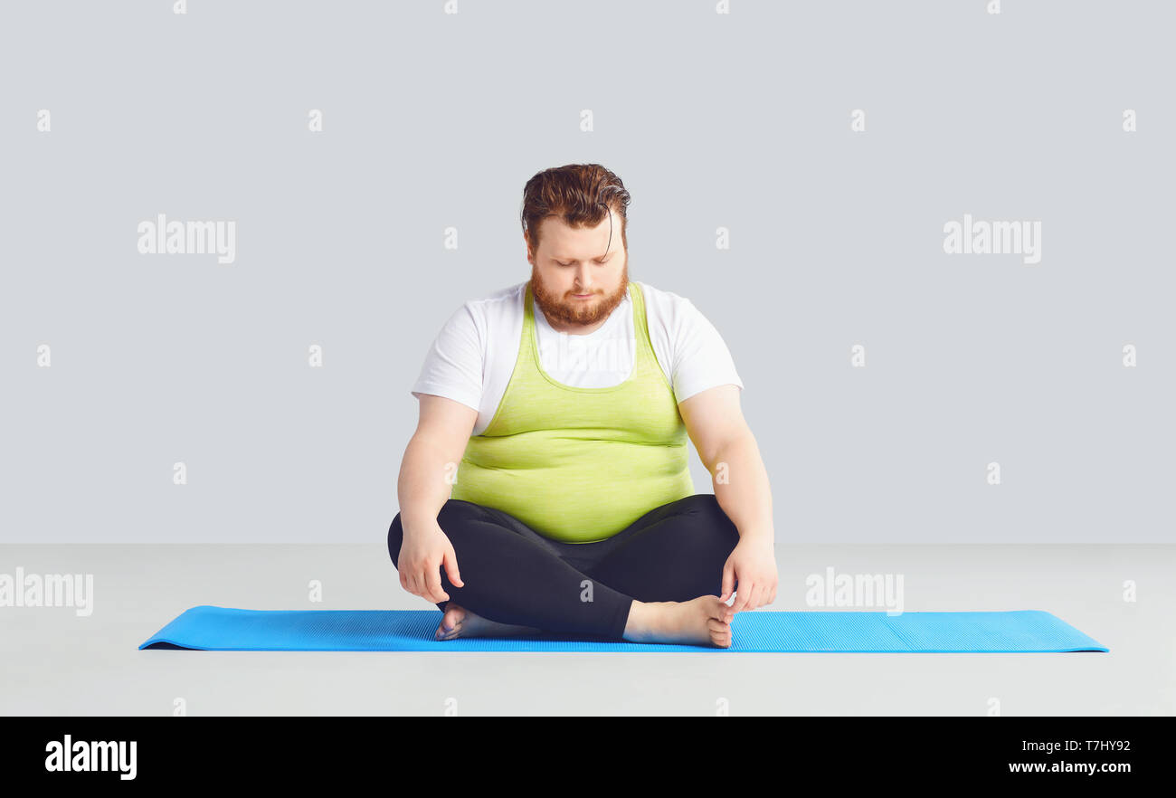 A fat unhappy man in yoga clothes on a gray background. Stock Photo