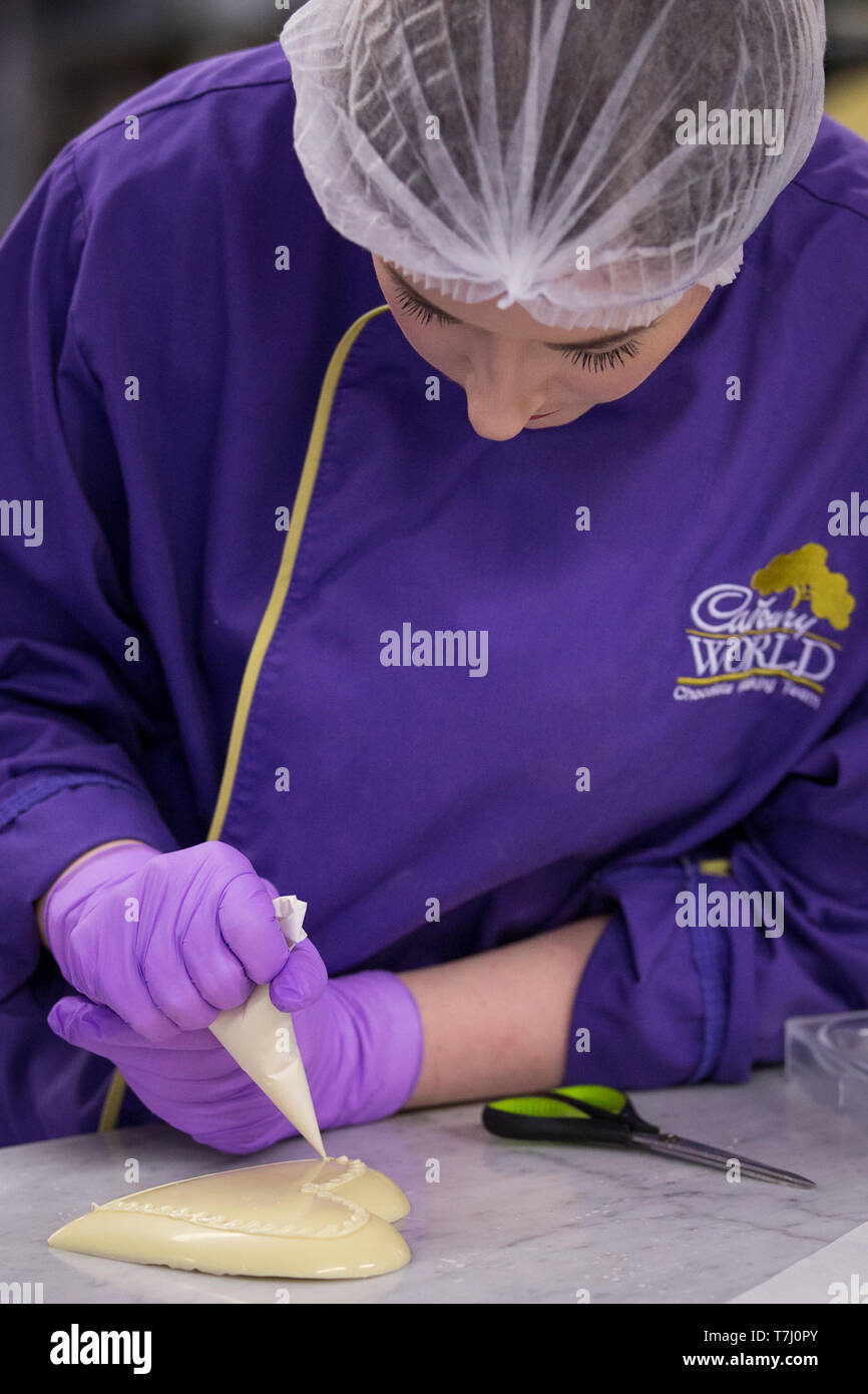 A chocolatier pipes white chocolate onto a heart for a giant chocolate teddy bear made for the announcement of a new royal baby at Cadbury World in Birmingham. Stock Photo