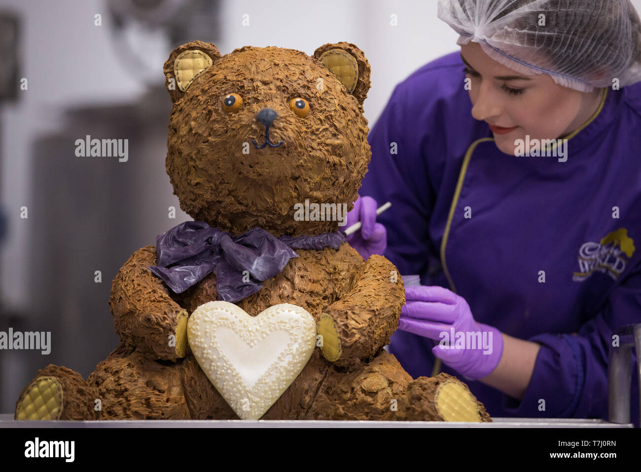 A chocolatier adds the finishing touches on a giant chocolate teddy bear made for the announcement of a new royal baby at Cadbury World in Birmingham. Stock Photo