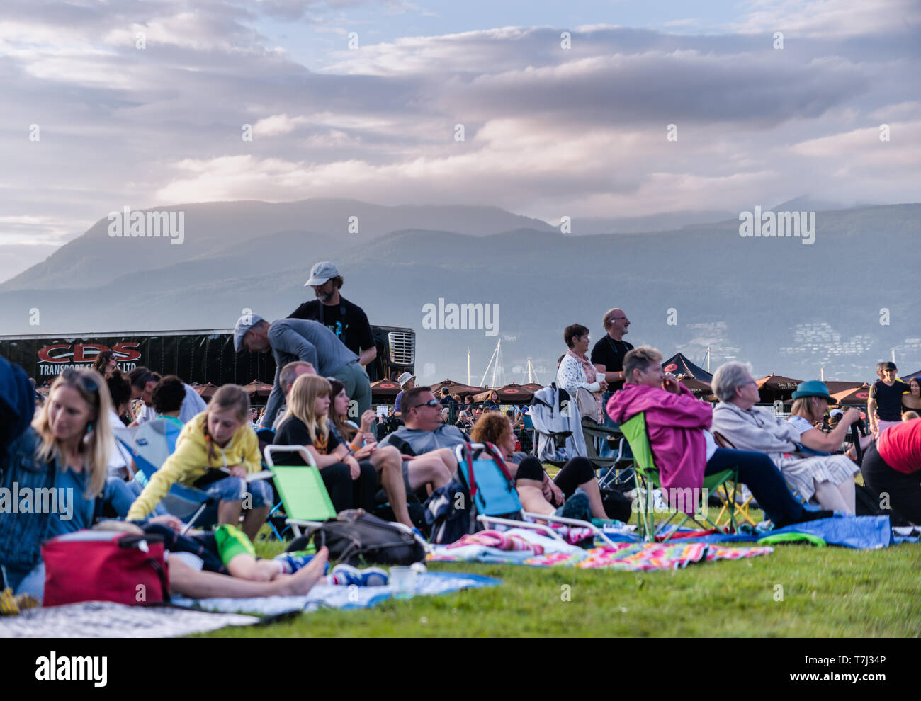 Audiences enjoy the dramatic outdoor setting of the Vancouver Folk Festival, with mountains and clouds in the background on a summer evening Stock Photo