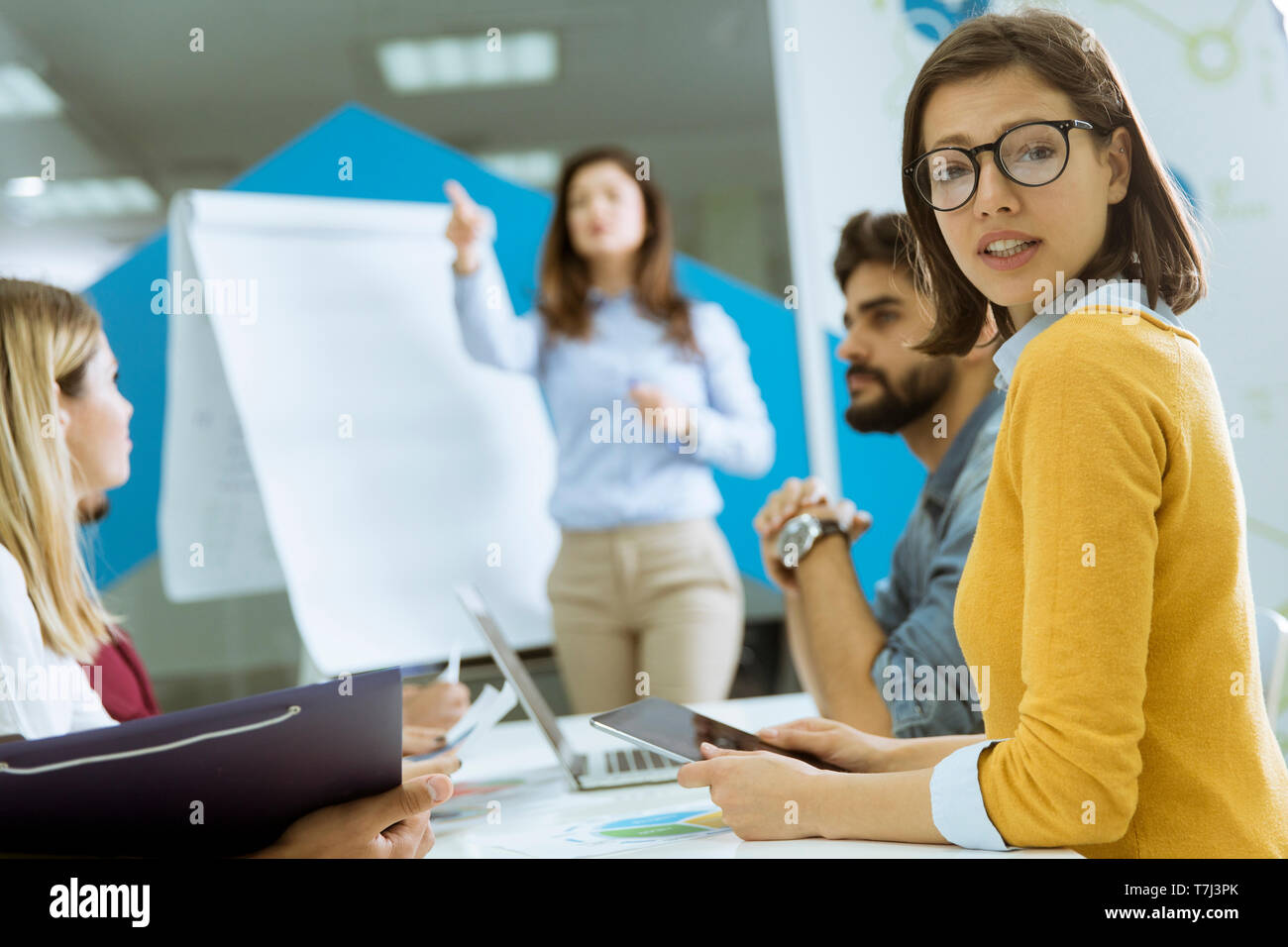 Confident young team leader giving a presentation to a group of young colleagues as they sit grouped by the flip chart in the small startup office Stock Photo