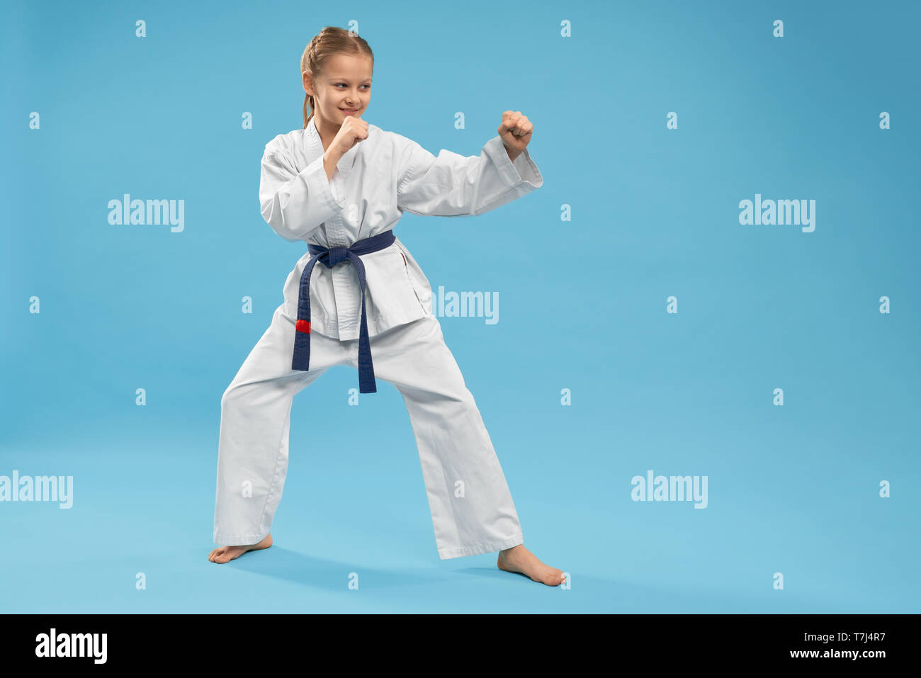 Side view of girl doing martial arts on blue isolated background