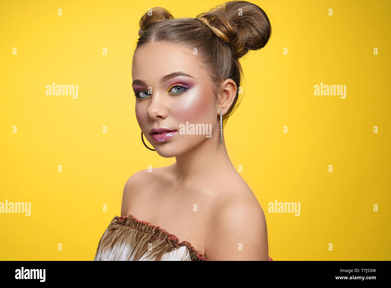 Side view of charming girl with great makeup looking at camera on yellow isolated background. Pretty female child with trendy hairstyle posing in studio. Concept of style and beauty. Stock Photo