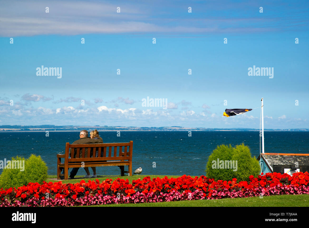 A Couple sat on a wooden Bench, St Andrews,St Andrews Bay, s, Fife, Scotland, UK. Stock Photo