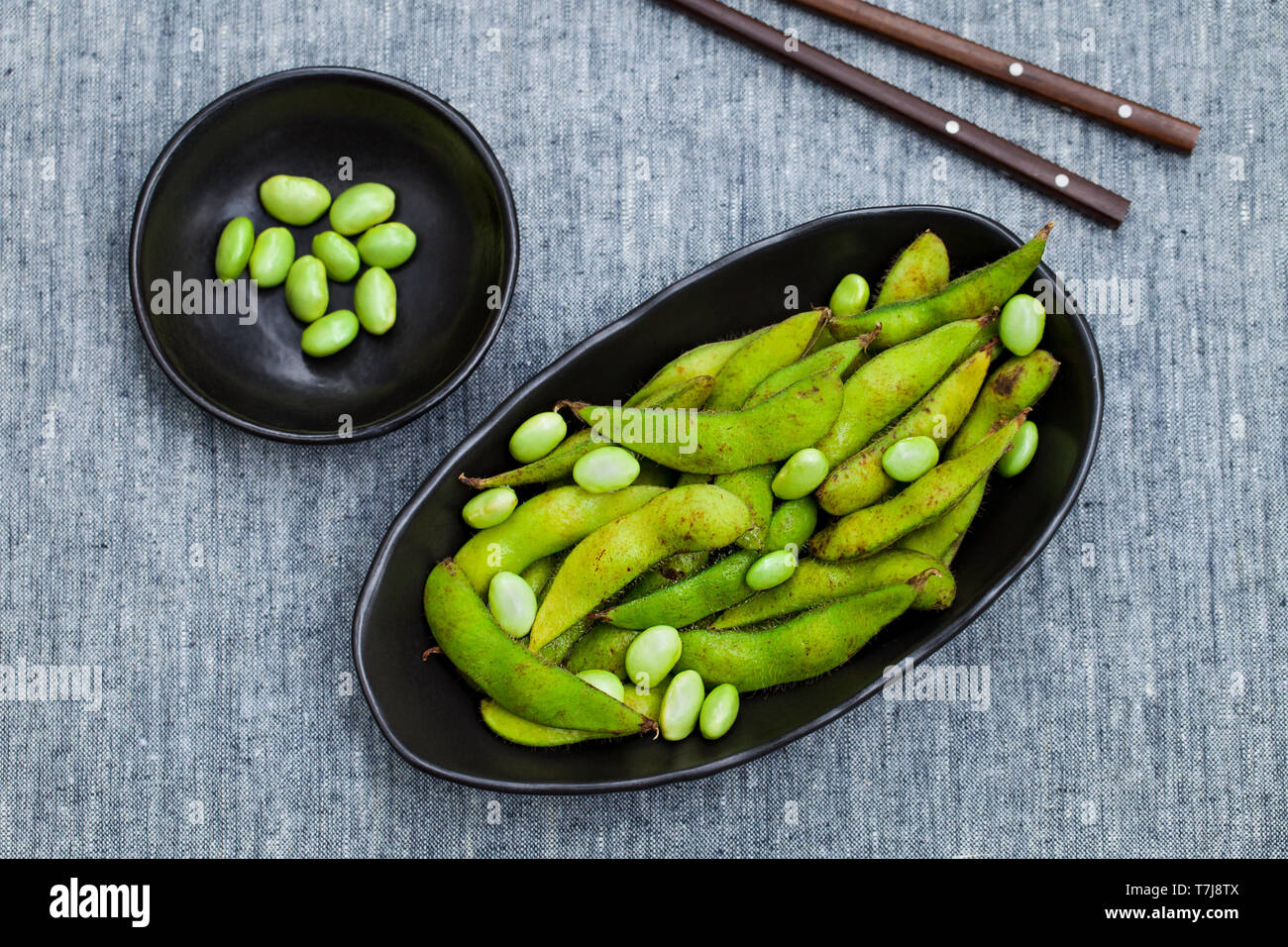 Fresh edamame green beans in black bowl. Grey background. Top view