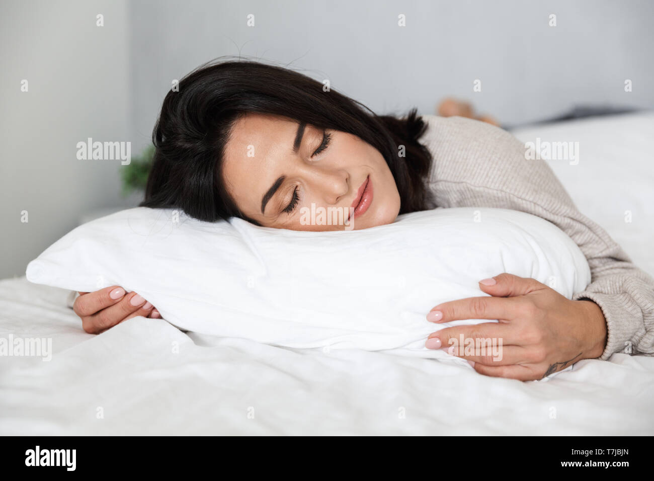 Photo of adult woman 30s sleeping while lying in bed with white linen at home Stock Photo