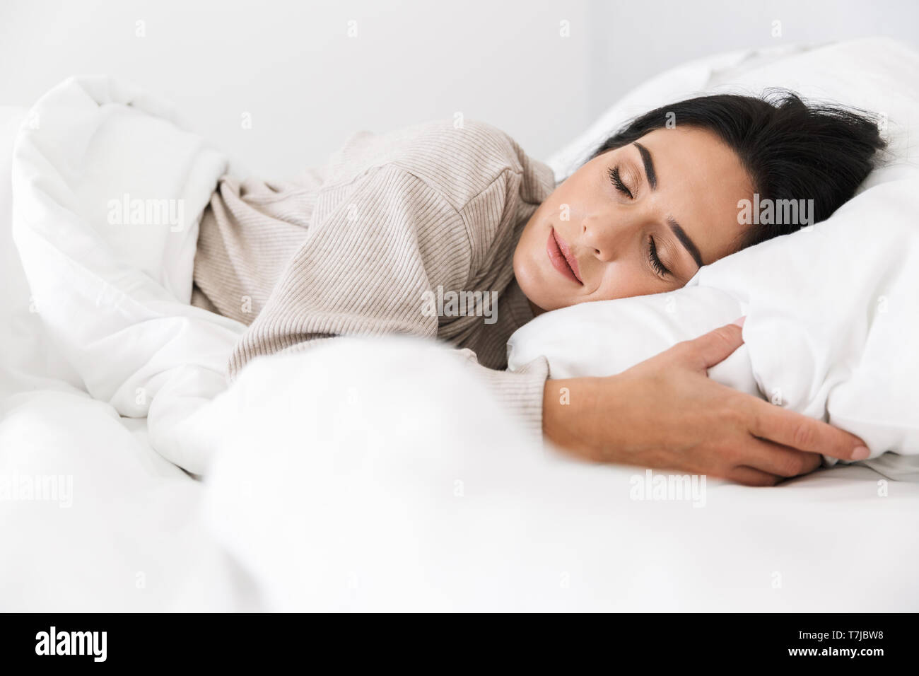 Photo of middle-aged woman 30s sleeping while lying in bed with white linen at home Stock Photo