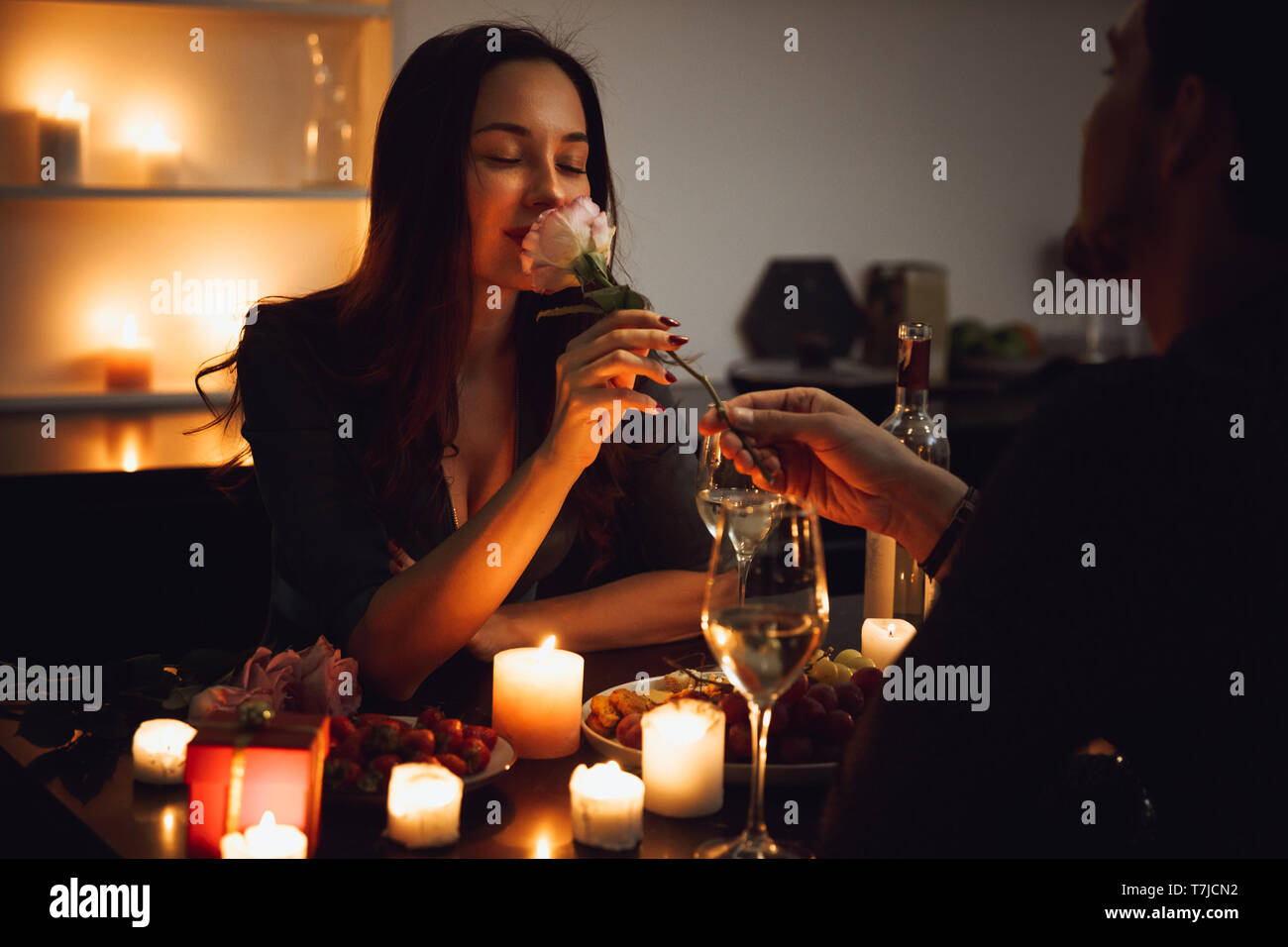 Beautiful passionate couple having a romantic candlelight dinner at home, woman smelling a