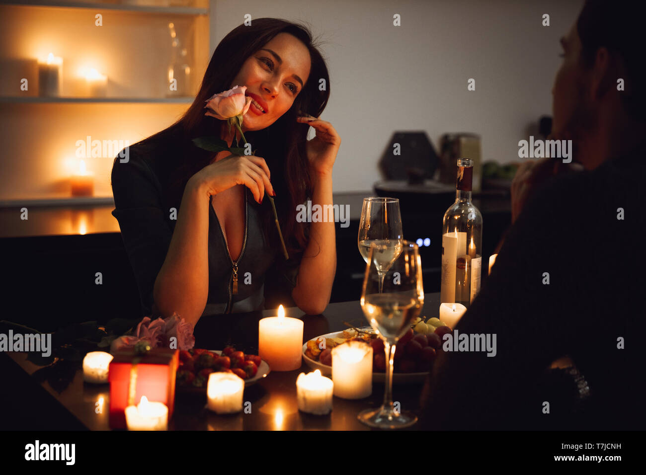 Beautiful passionate couple having a romantic candlelight dinner at home, woman smelling a