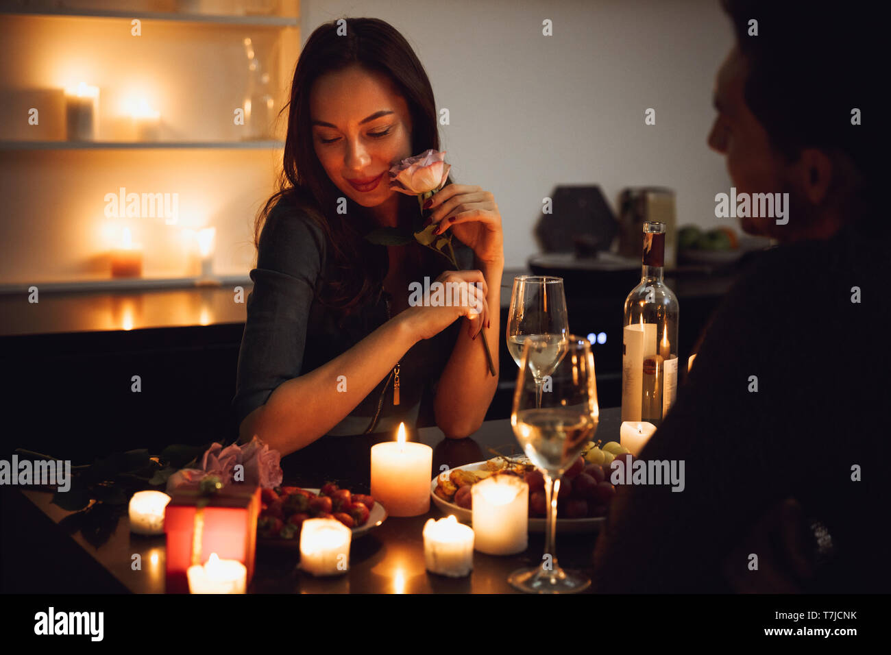 Beautiful passionate couple having a romantic candlelight dinner at home, woman smelling a