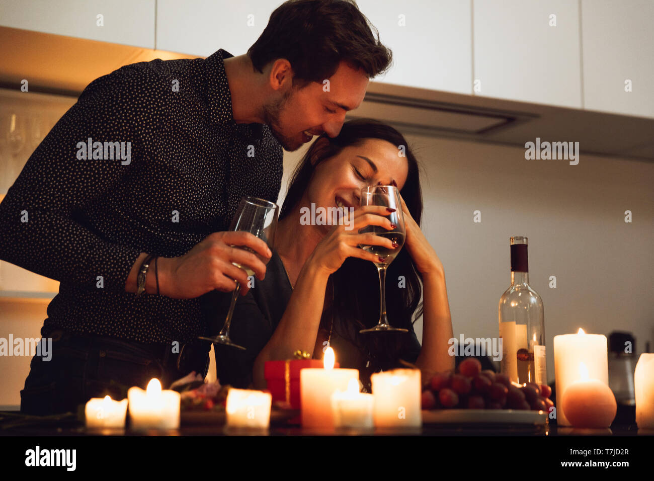 Beautiful passionate couple having a romantic candlelight dinner at home, kissing Stock Photo