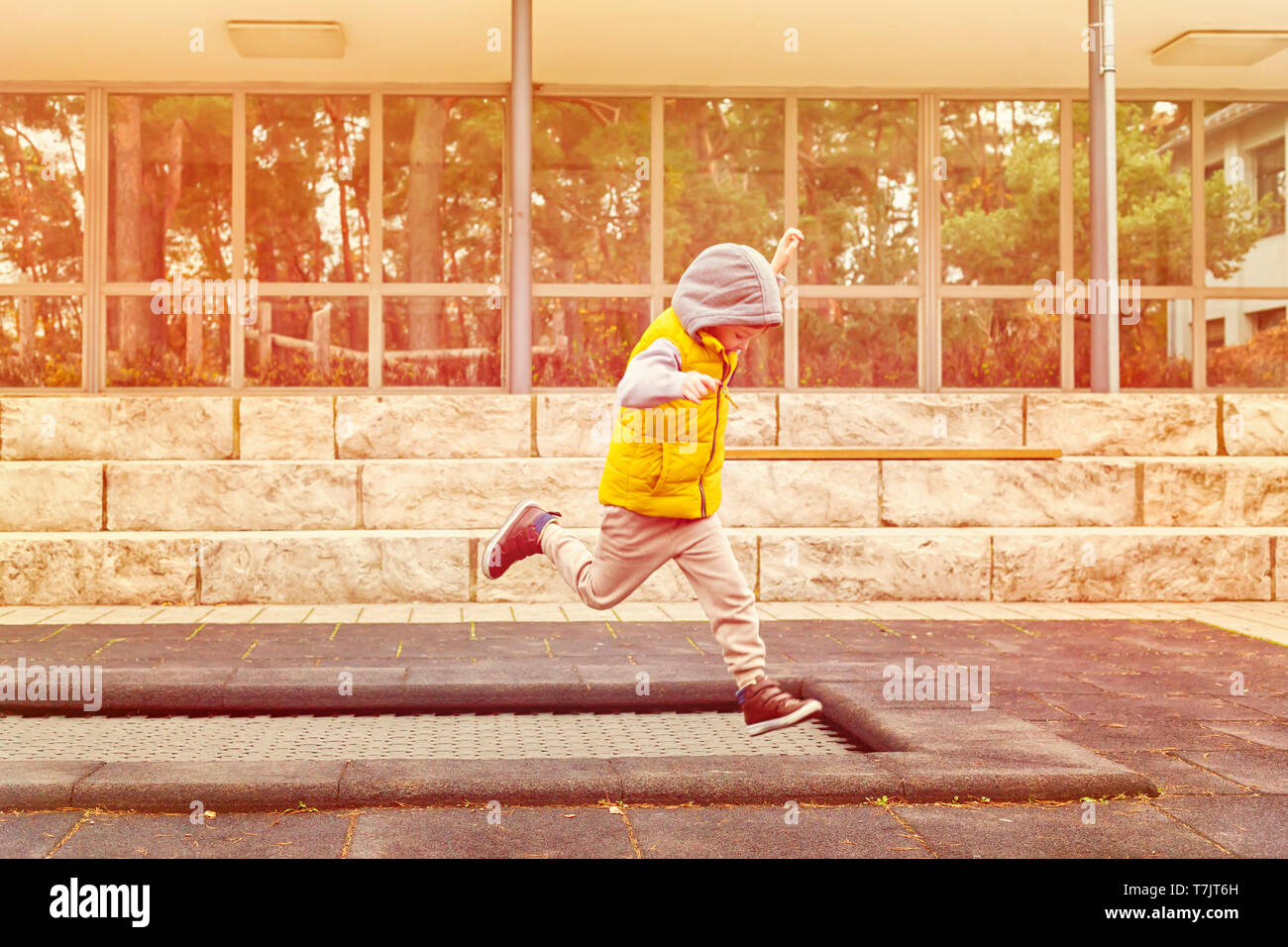 Happy child, active five year old boy plays outdoors in playground jumping high in the sky on trampoline Stock Photo