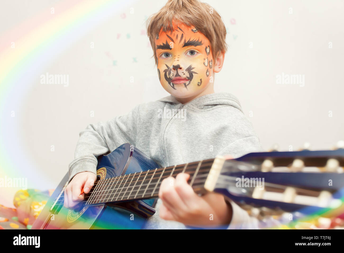 Little five year old boy with leopard face paint playing guitar on