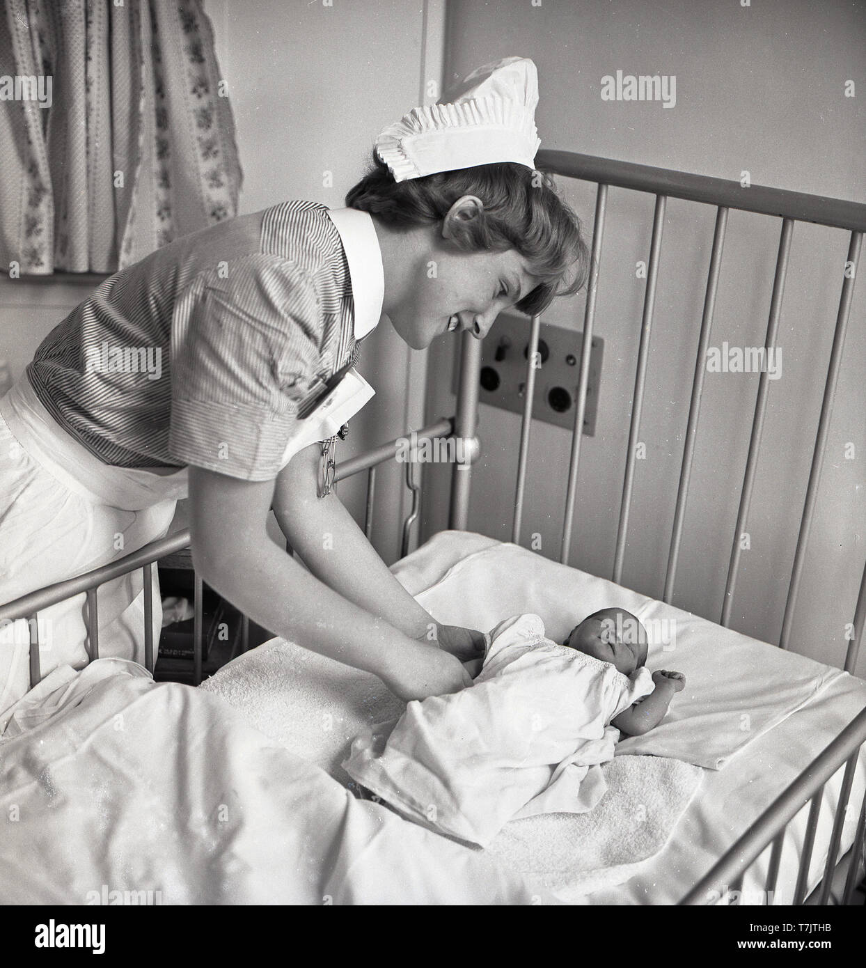 1960s, historical, a female nurse checking on a small newly born baby asleep on a metal hospital cot, England, UK. Stock Photo