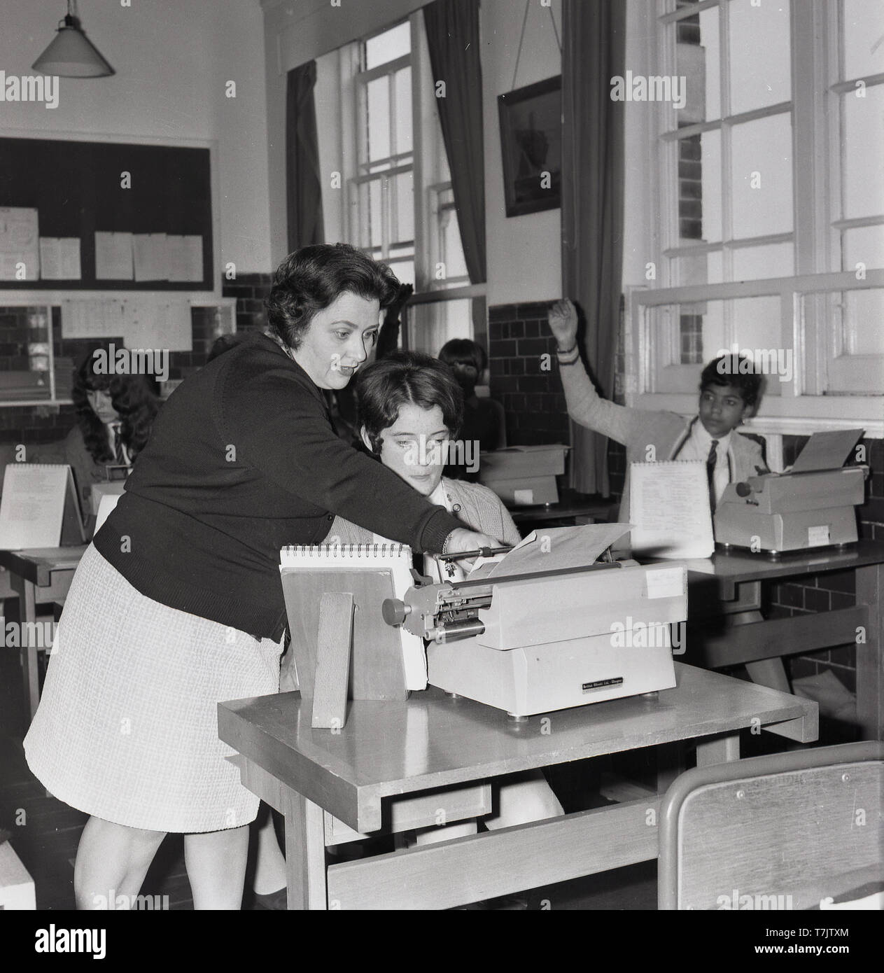 1960s, historical, lady teacher in a classroom helping a girl with her typing, London, England, UK. Stock Photo