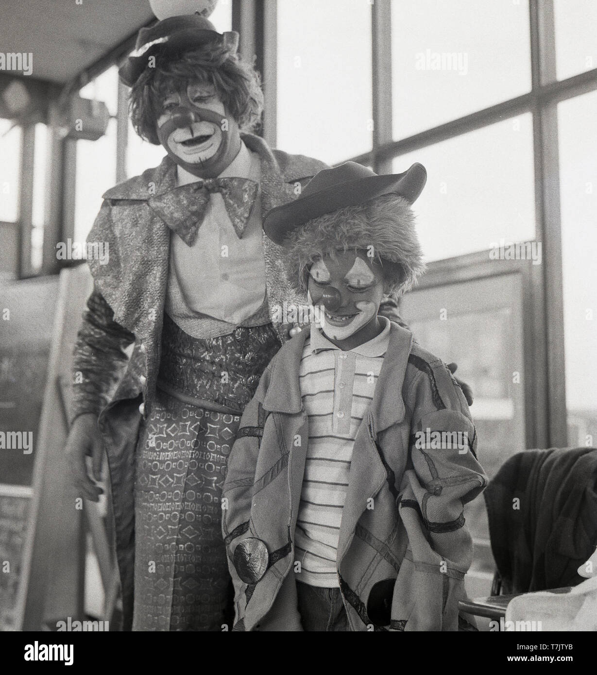 1960s, historical, a circus clown visting a primary school with a young schoolboy wearing fancy dress and with his face painted as a clown, England, UK. Stock Photo