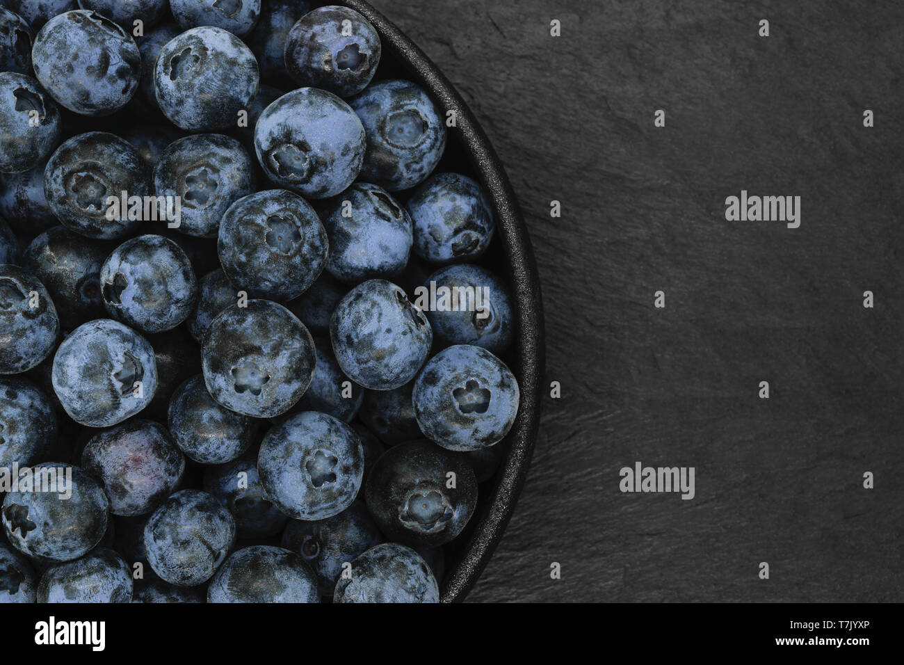 Blueberries in round and black cast iron bowl on black stone background with copy space Stock