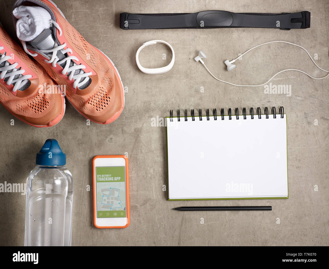 Closeup on sneakers, heart rate monitor, bottle of water, white fitness tracker, headphones, smartphone with gps activity tracking app and opened note Stock Photo