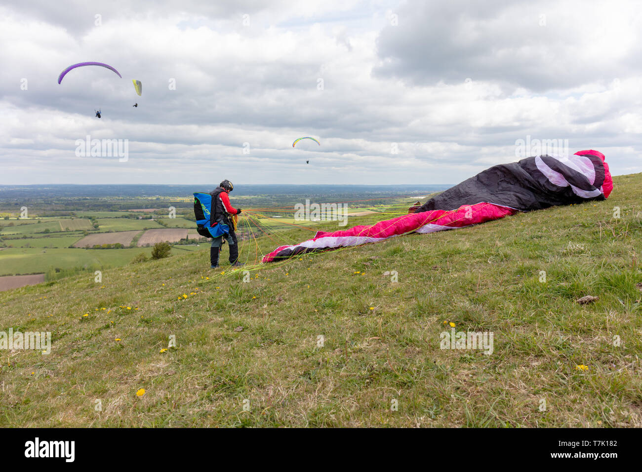 Devils Dyke, Sussex, UK; 6th May 2019; Male Paraglider Standing Next to his Collapsed Canopy. Three Paragliders Flying in the Background Stock Photo