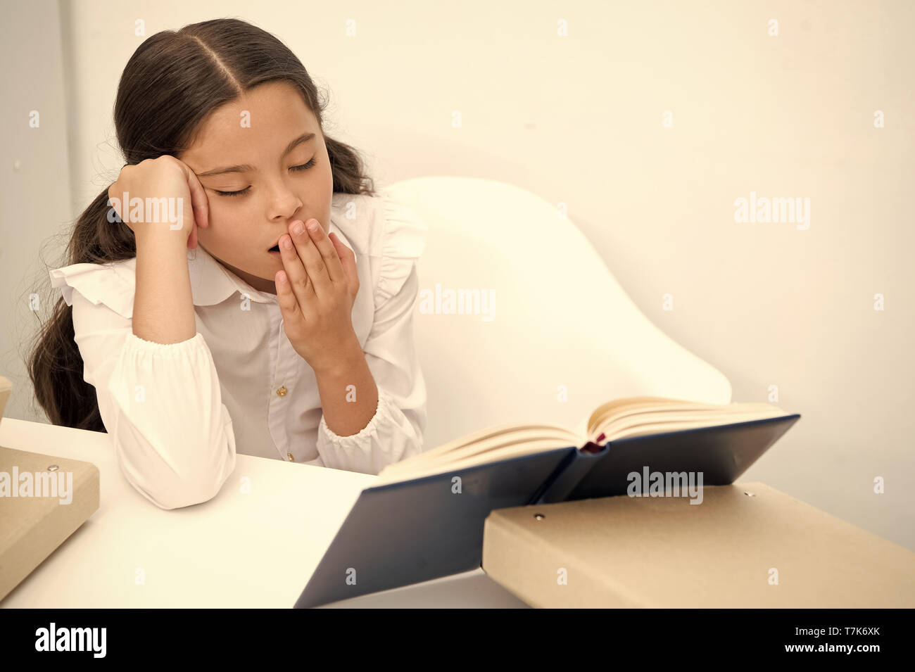 Boring literature. Girl child reads book while sit table white