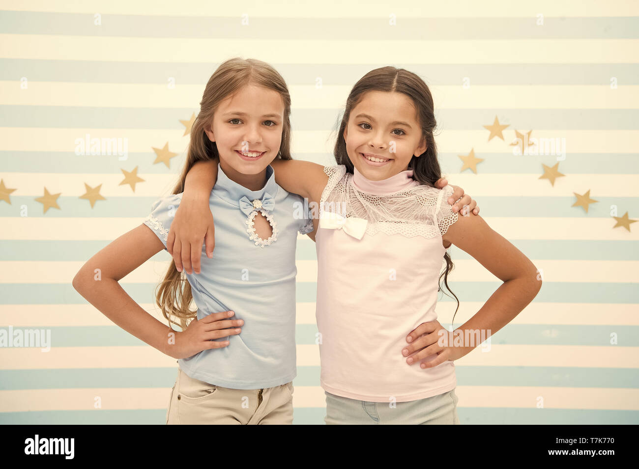 Happy childhood concept. Kids schoolgirls preteens happy together. Friendship from childhood. Girls smiling happy faces hug each other while stand striped background. Girls children best friends hugs. Stock Photo