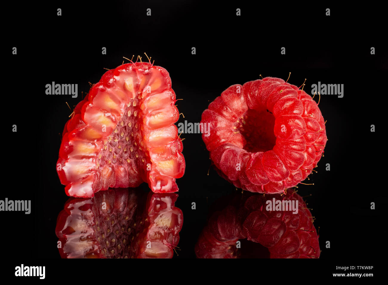 Group of one whole one half of fresh red raspberry cross section isolated on black glass Stock Photo