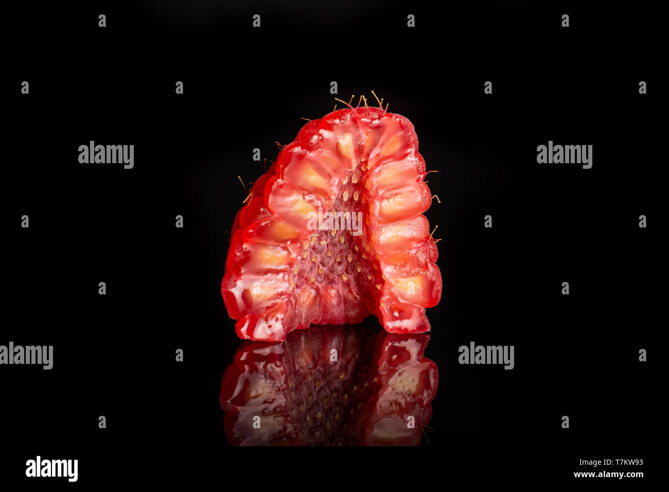 One half of fresh red raspberry cross section isolated on black glass Stock Photo