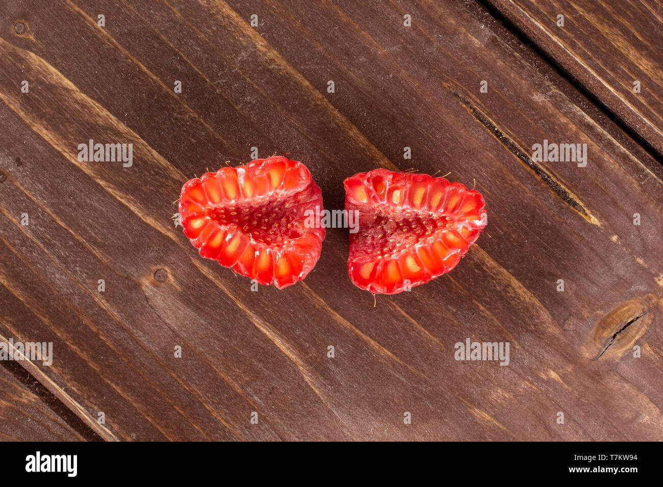 Group of two halves of fresh red raspberry cross section flatlay on brown wood Stock Photo