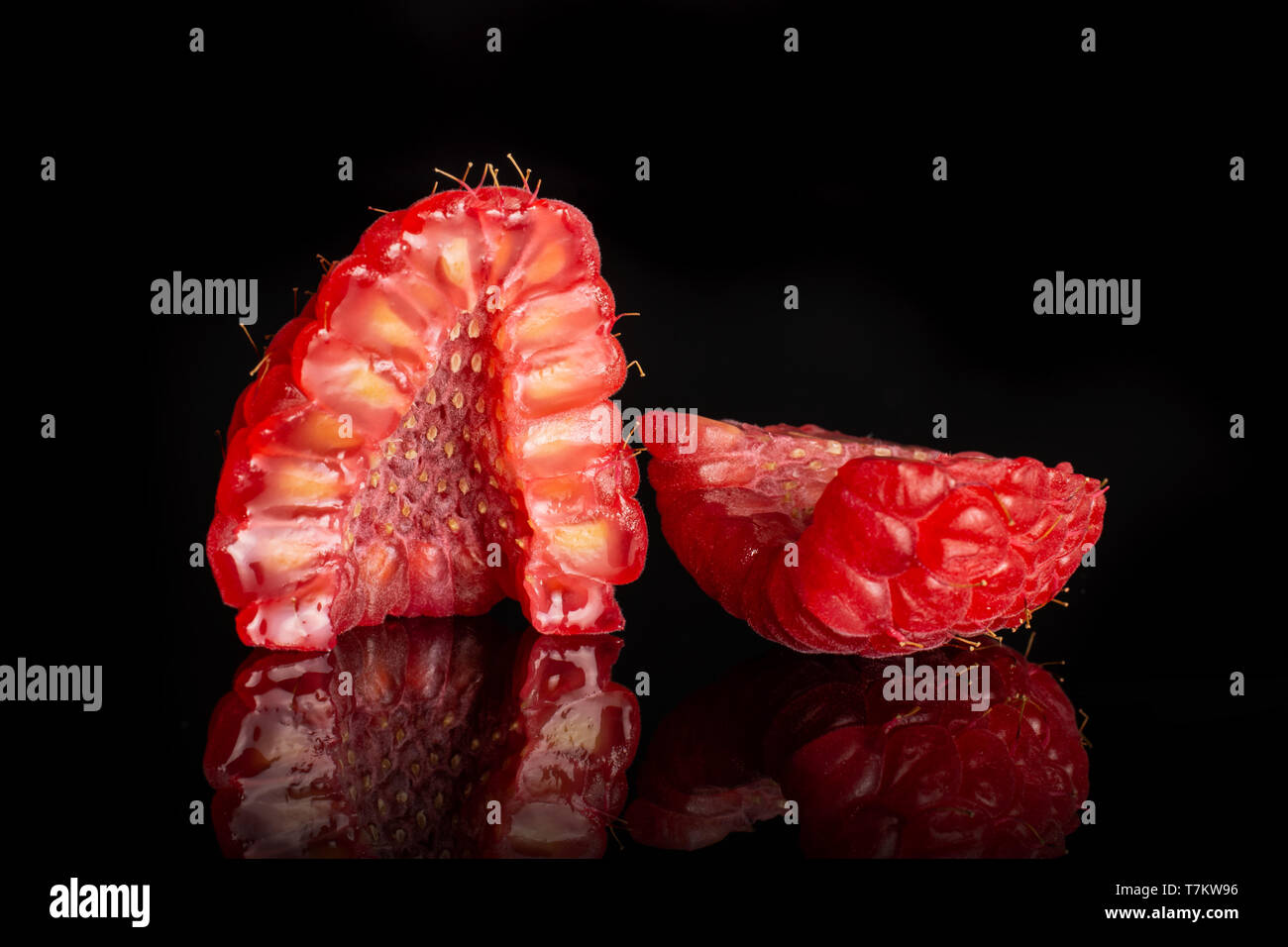 Group of two halves of fresh red raspberry one cut in a cross section isolated on black glass Stock Photo