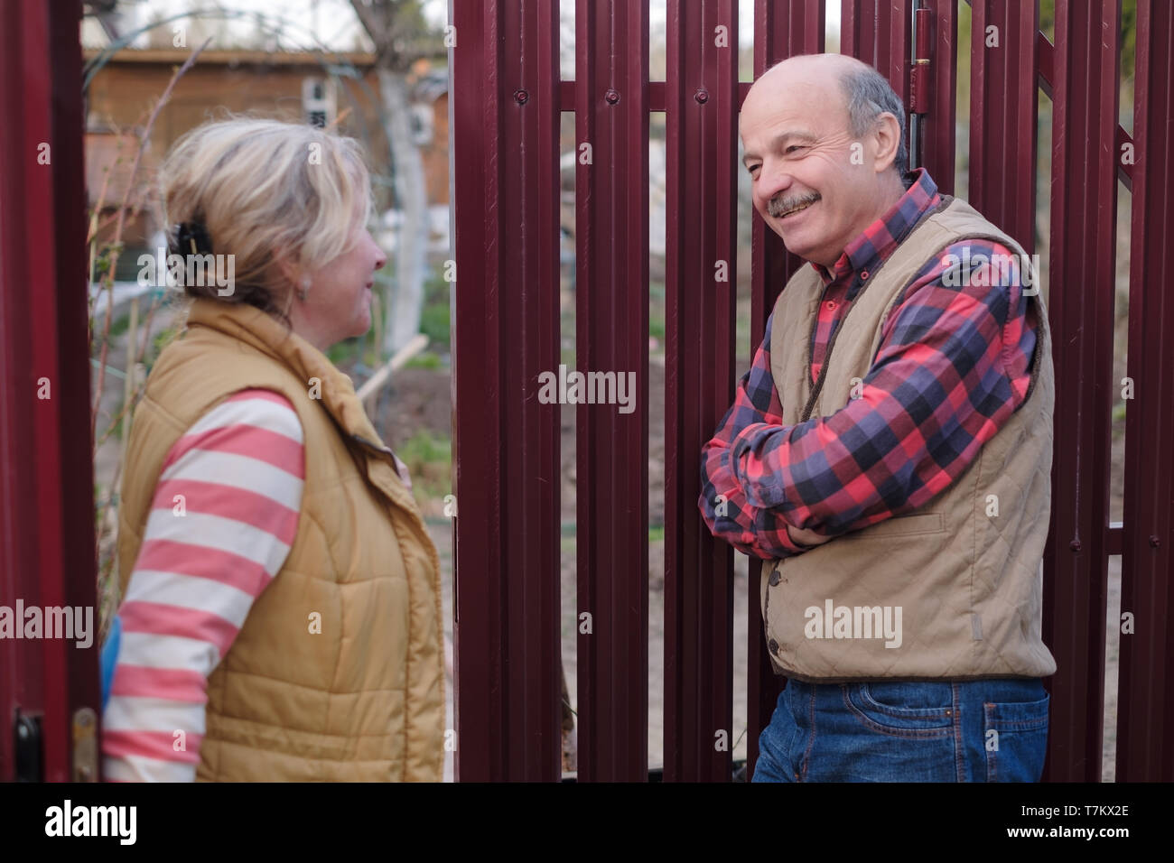 Two senior neighbors takling to each other on sunny day near fence. Stock Photo