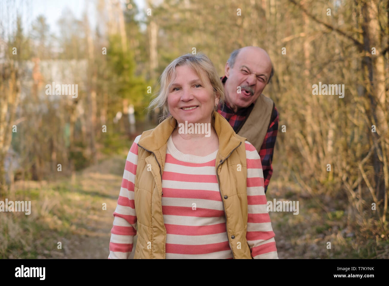 Mature woman smiling standing outdoor. Her husband teasing her showing tongue. Stock Photo
