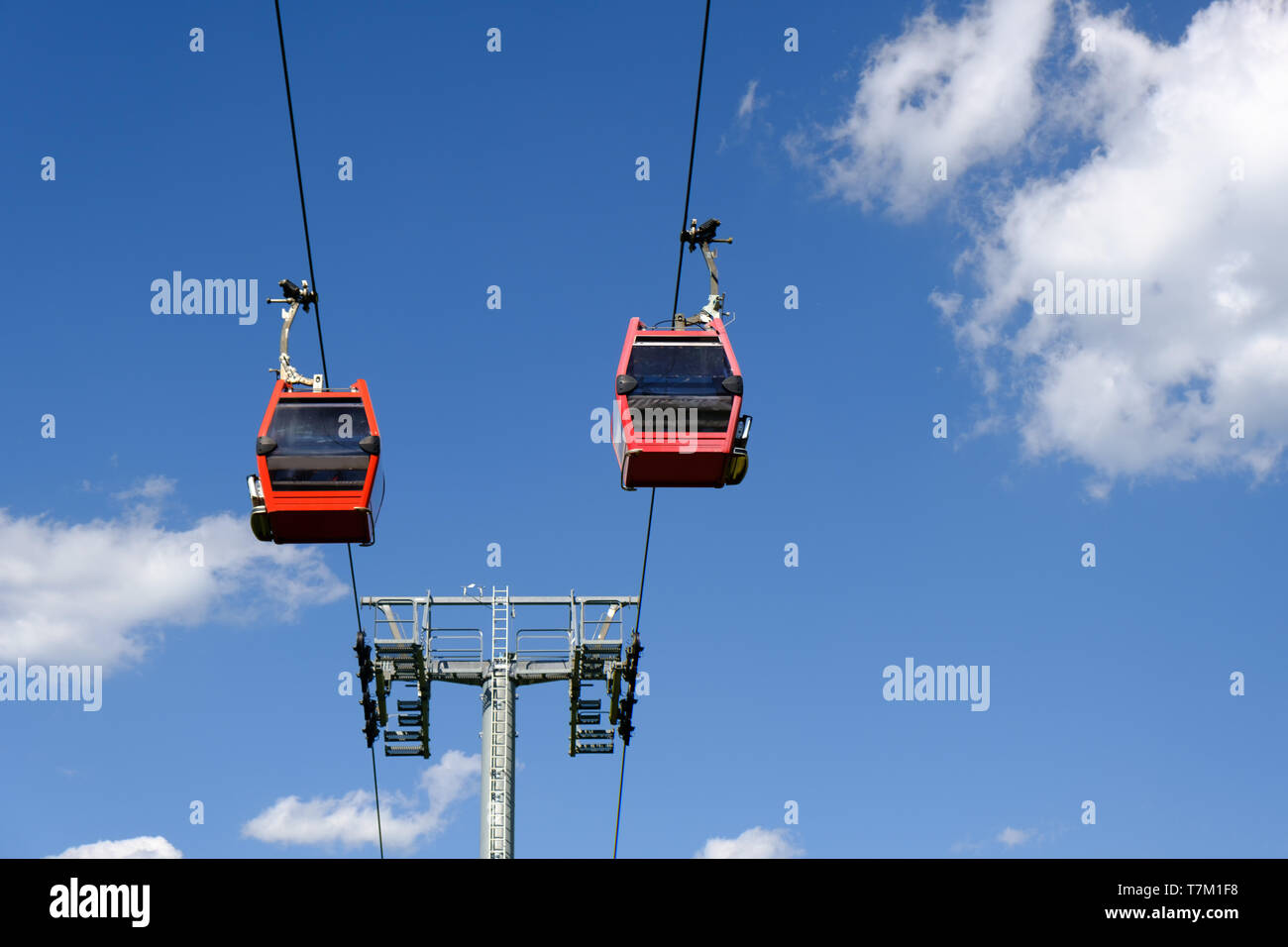 Two cable cars suspended in air agains blue sky with white puffy clouds, ski lift, no people Stock Photo