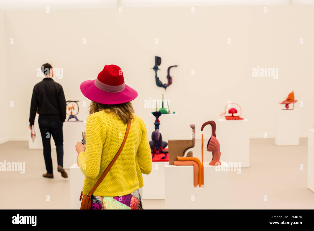 New York, NY - May 3, 2019. A woman in a bright hat and yellow jacket in the midst of Matthew Ronay's sculptures in the Casey Kaplan Gallery at the Frieze Art Fair on New York City's Randalls Island. Stock Photo