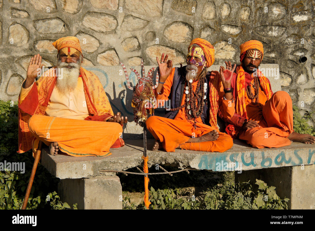 Three sadhus (holy men) with painted faces, clad in orange robes, sit on a bench at Pashupatinath Hindu temple, Kathmandu Valley, Nepal Stock Photo