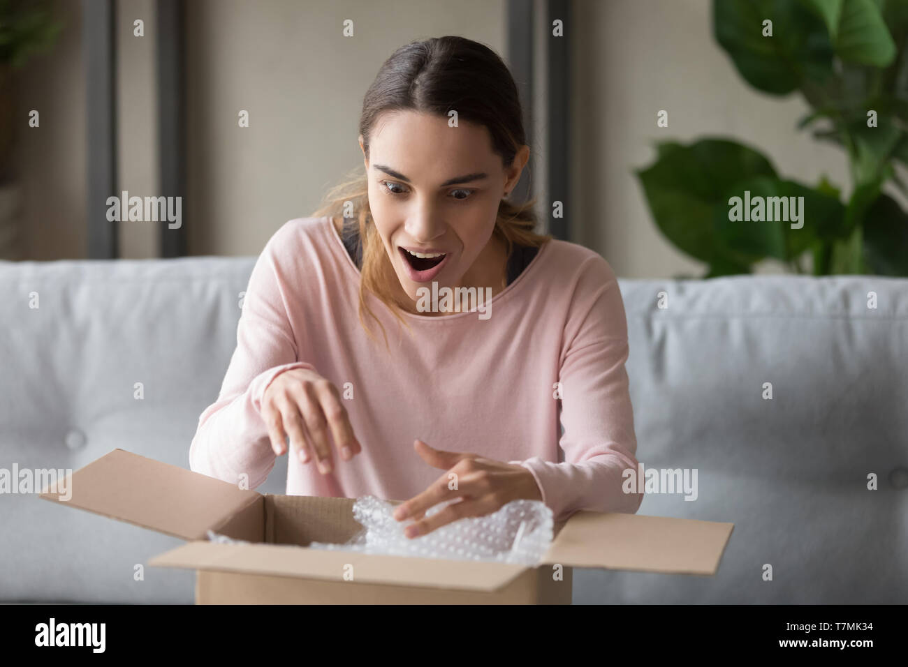 Surprised woman unpacks carton box at home feels happy Stock Photo