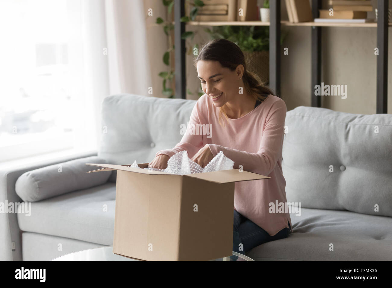 Client woman sitting on couch unbox carton box feels satisfied Stock Photo