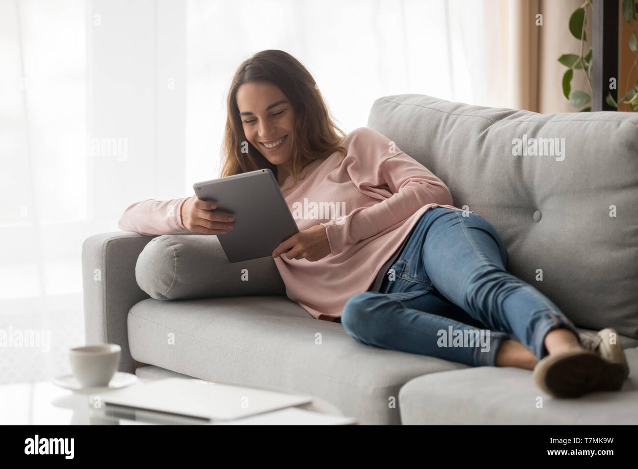 Woman lying on couch with tablet spending time at home Stock Photo