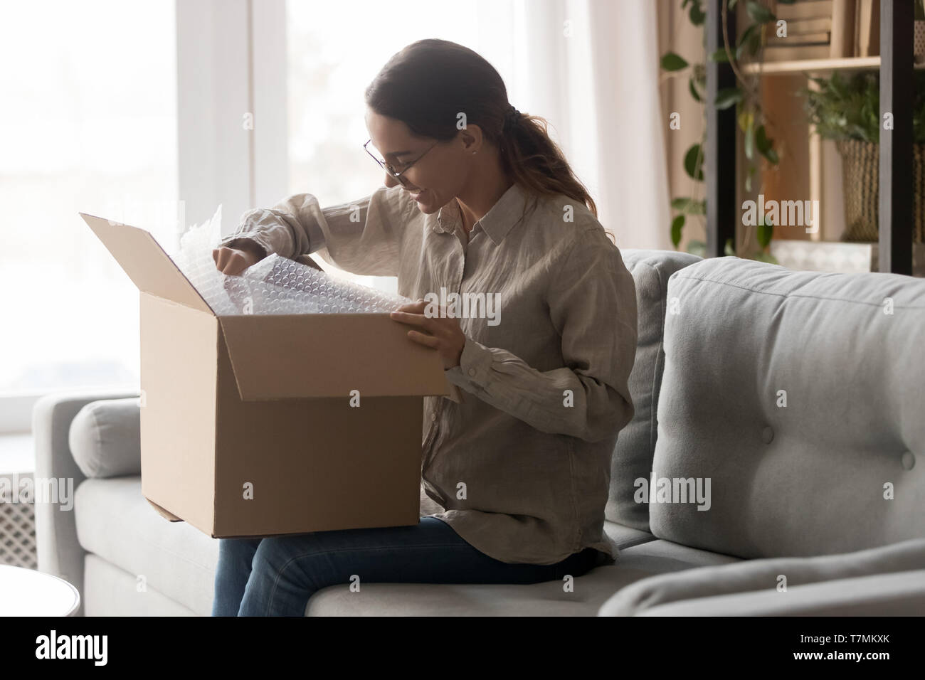 Woman holds big carton box on laps unpack delivered goods Stock Photo